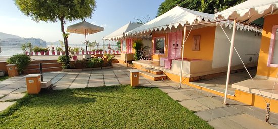 Outdoor seating area with pink and white tents by a riverside, adorned with potted plants, under clear skies.