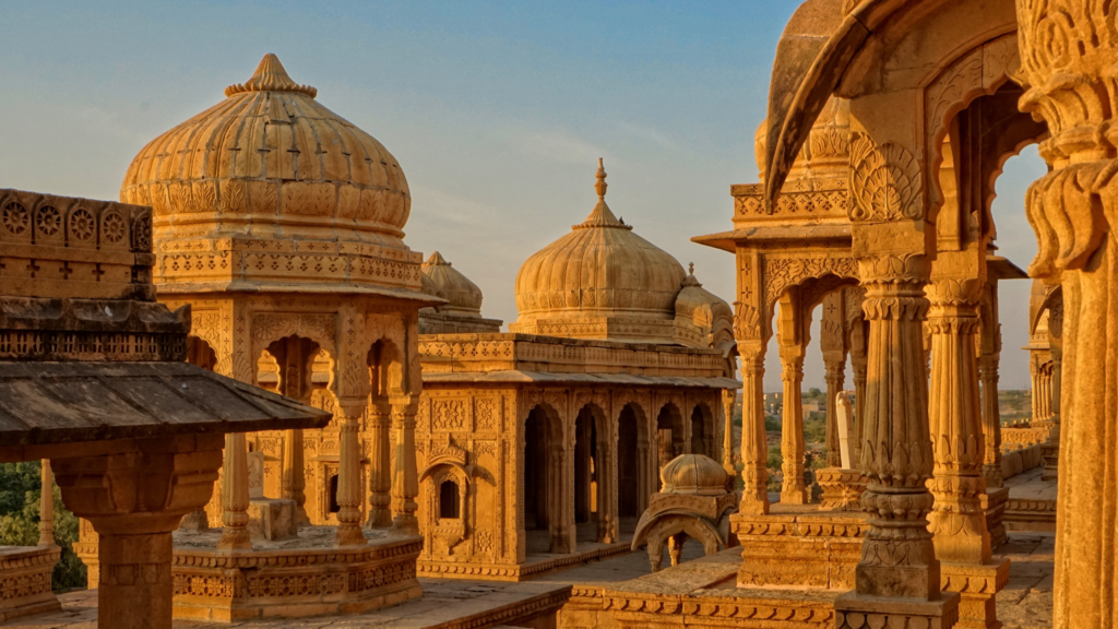 Sunset casts a warm glow on the intricately carved domes and arches of ornate sandstone structures at the Bada Bagh cenotaph complex in Jaisalmer, India.