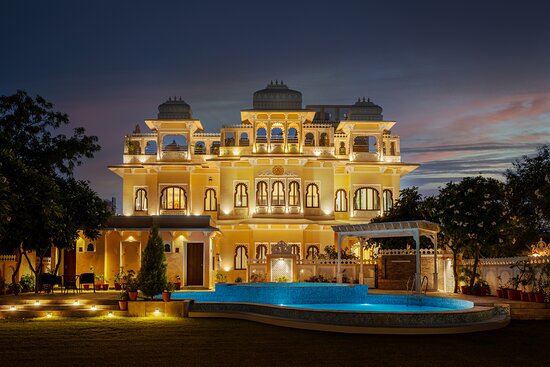 An illuminated traditional indian palace with ornate arches and domes, set against a twilight sky, featuring a pool and garden lights.