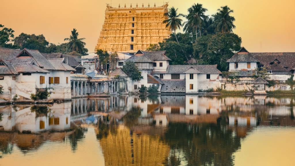 The image shows the golden facade of the Padmanabhaswamy Temple with its reflection in a nearby water body, surrounded by traditional buildings and lush palm trees at sunset.