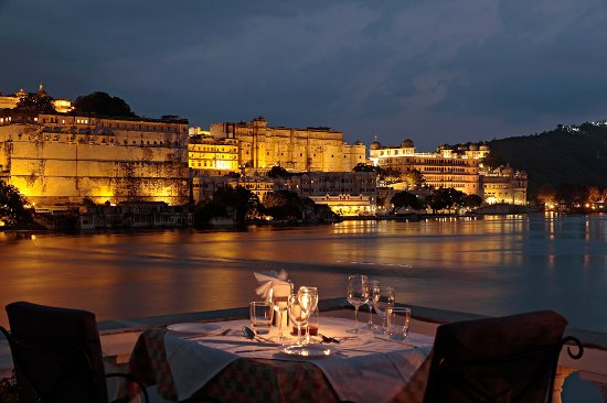 A romantic dinner setup with a view of a brightly lit palace and lake at dusk.