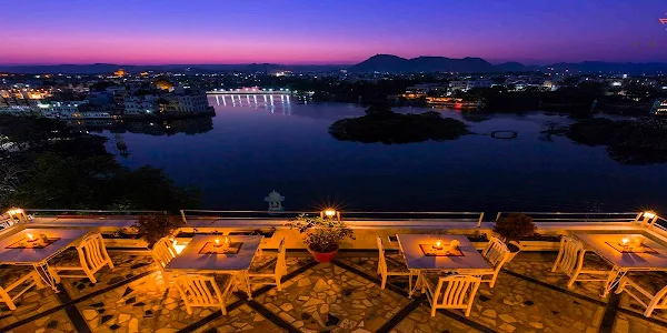 Outdoor restaurant terrace overlooking a serene lake and cityscape during twilight, with tables set for dining.