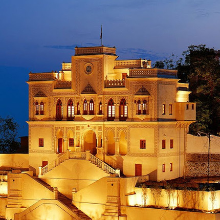 The illuminated yellow building with intricate architectural details, set under a twilight sky and surrounded by trees, resembles one of the best destination wedding resorts in India, offering an enchanting ambiance perfect for unforgettable celebrations.