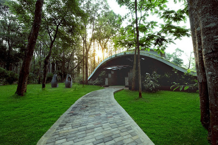 A curved pathway leads to a modern building with a green roof, surrounded by trees and grass, reminiscent of the best destination wedding resorts in India.